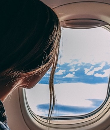 Voyage vers la Corse avec Air Corsica | KDriver Corse Transfert Aéroport Cliente regardant par le hublot de son vol Air Corsica, en route vers la Corse pour un transfert KDriver Corse.