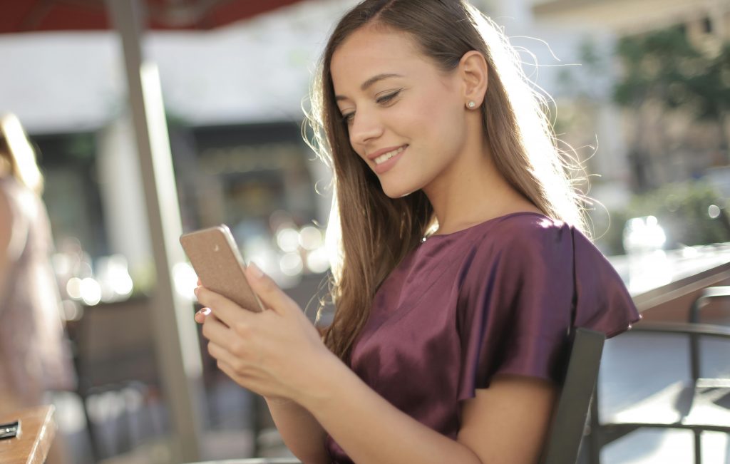 Réservation Chauffeur VTC via App Mobile | KDriver Corse Femme souriante réservant un chauffeur VTC sur son smartphone via l'application mobile KDriver Corse.